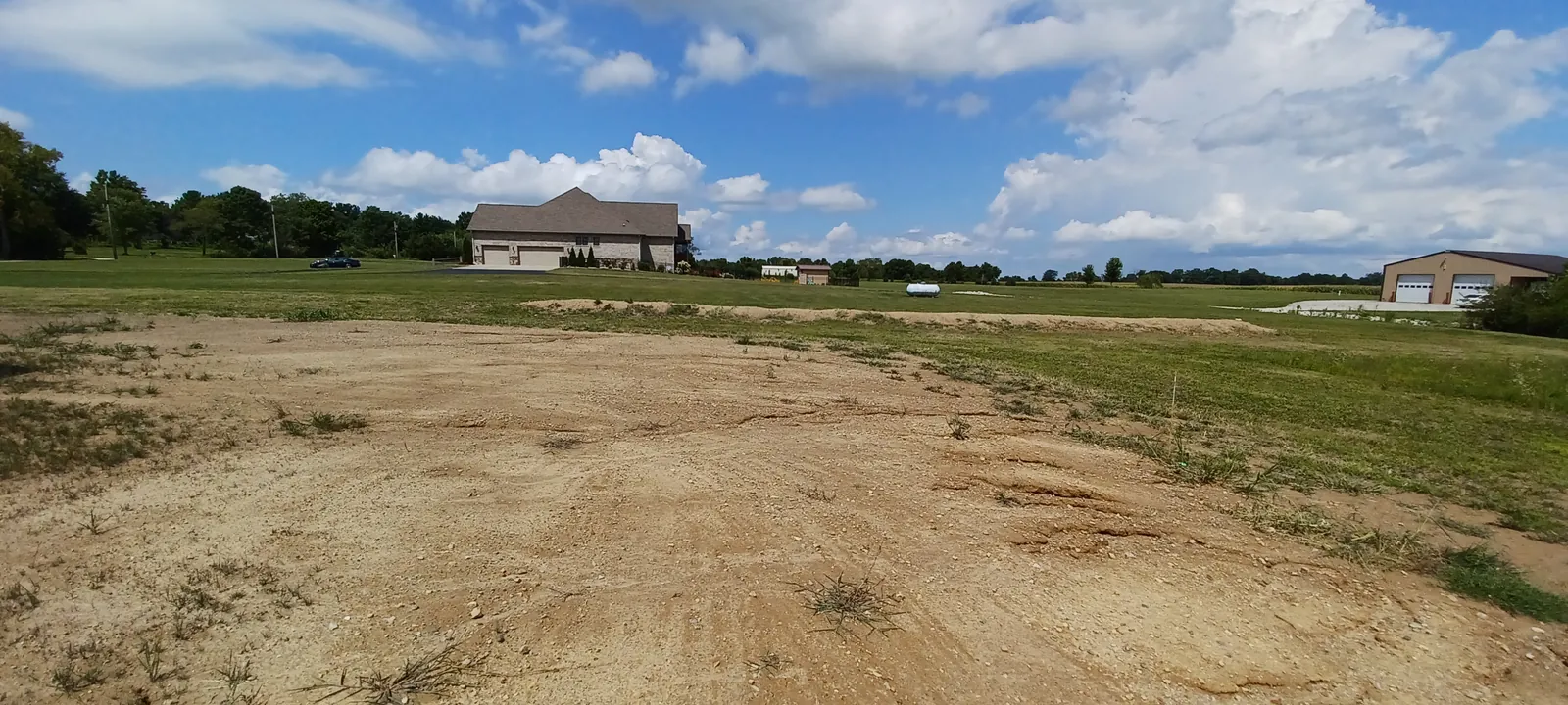 Wide lot graded flat and smooth in an open field, with homes in the distance