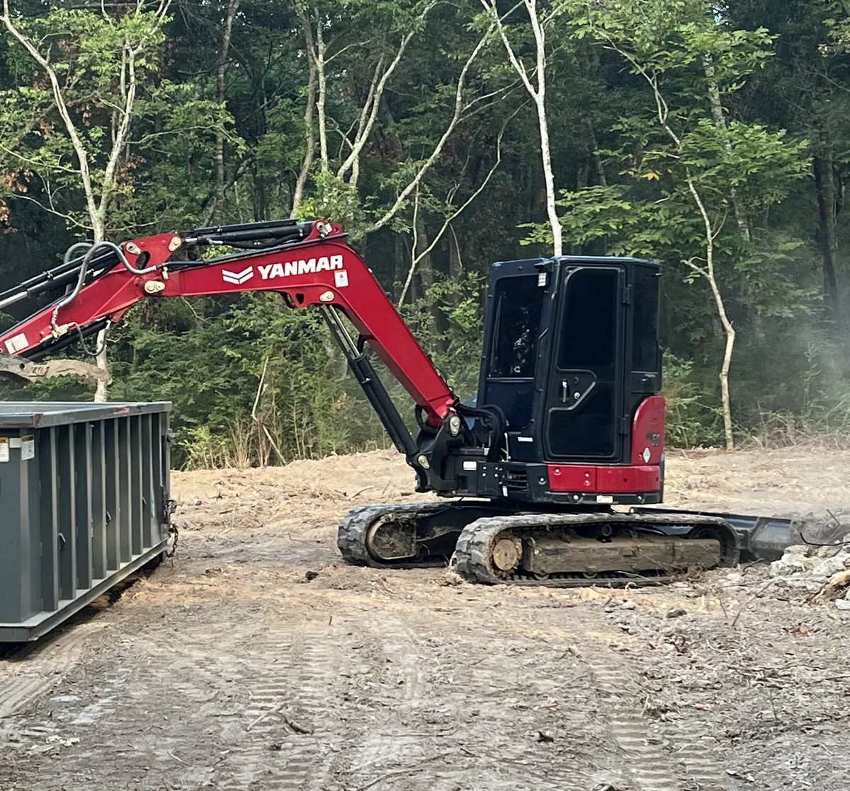 Mini excavator loading broken material into a roll-off container on a cleared lot